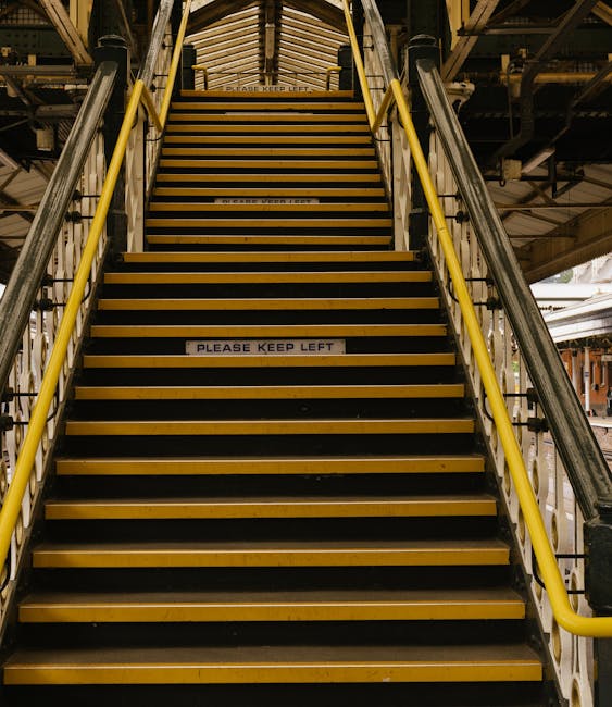 The image shows a view of North Dulwich station platform during daytime, with the station's elevated structure featuring white scalloped decorative trim beneath the roof. A large green and yellow sign